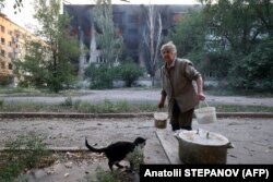 Local resident Tetyana, 72, feeds a cat in front of a burning apartment building after shelling in the town of Toretsk, Donetsk region, on July 29.