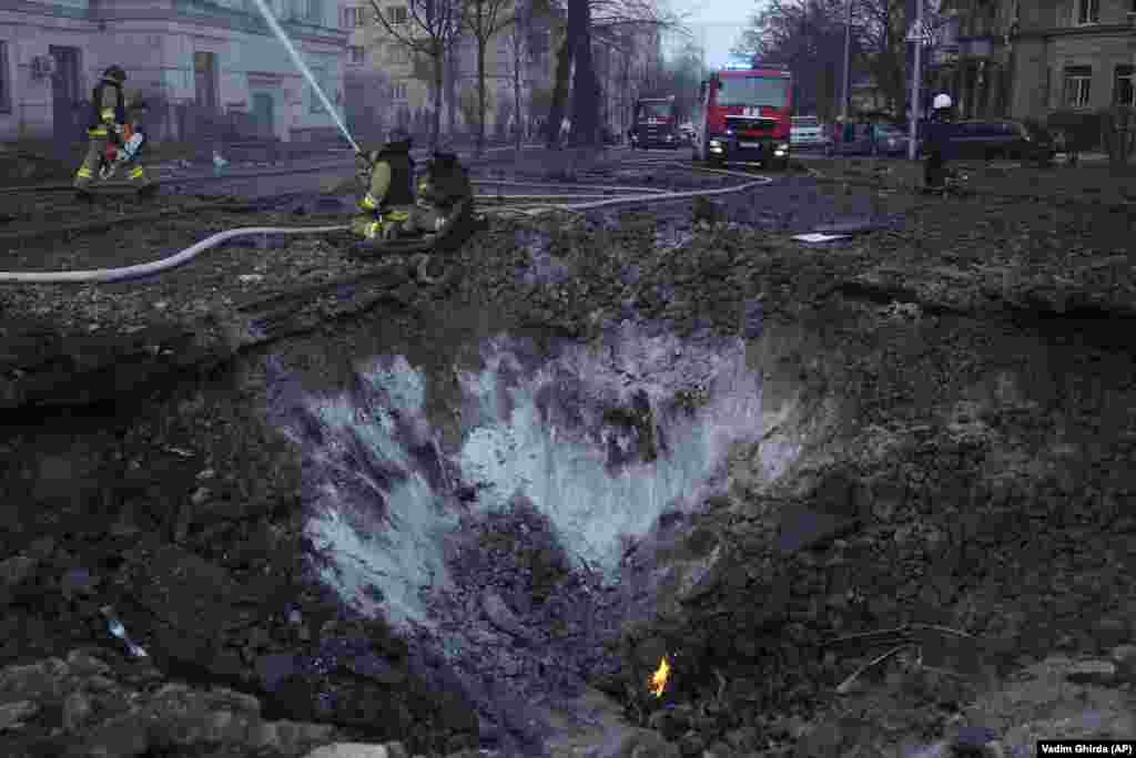 Pompierii în acțiune în apropierea unui crater format de explozia unei rachete rusești, în urma atacului asupra Kievului. Primele informații sugerau că sunt pagube în cel puțin trei sectoare ale Kievului, inclusiv în zone rezidențiale.