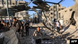 Момче трча со вреќа додека луѓето ги пребаруваат урнатините на урнатата зграда како последица на израелското бомбардирање во училиштето Џауни, управувано од Агенцијата за помош и работа на ОН за палестинските бегалци. 