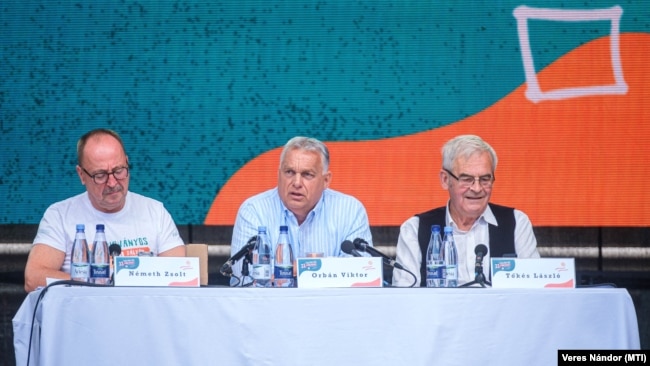 Orbán Viktor miniszterelnök (k) előadást tart a Tusnádfürdőn 2024. július 27-én. Mellette Németh Zsolt, az Országgyűlés külügyi bizottságának fideszes elnöke (b) és Tőkés László, az Erdélyi Magyar Nemzeti Tanács (EMNT) elnöke (j)
