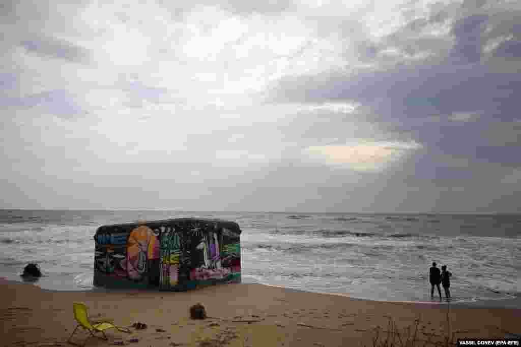 Tourists look out to the stormy sea next to a German military bunker from World War II on the northern part of Black Sea beach in the village of Ezerets, Bulgaria.