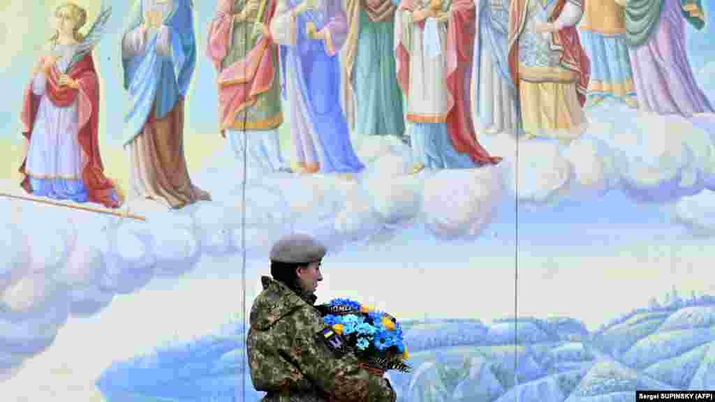 Ukrajinska vojnikinja nosi cvijeće u bojama ukrajinske zastave u Kijevu na sahranu vojnika poginulog u borbi.
