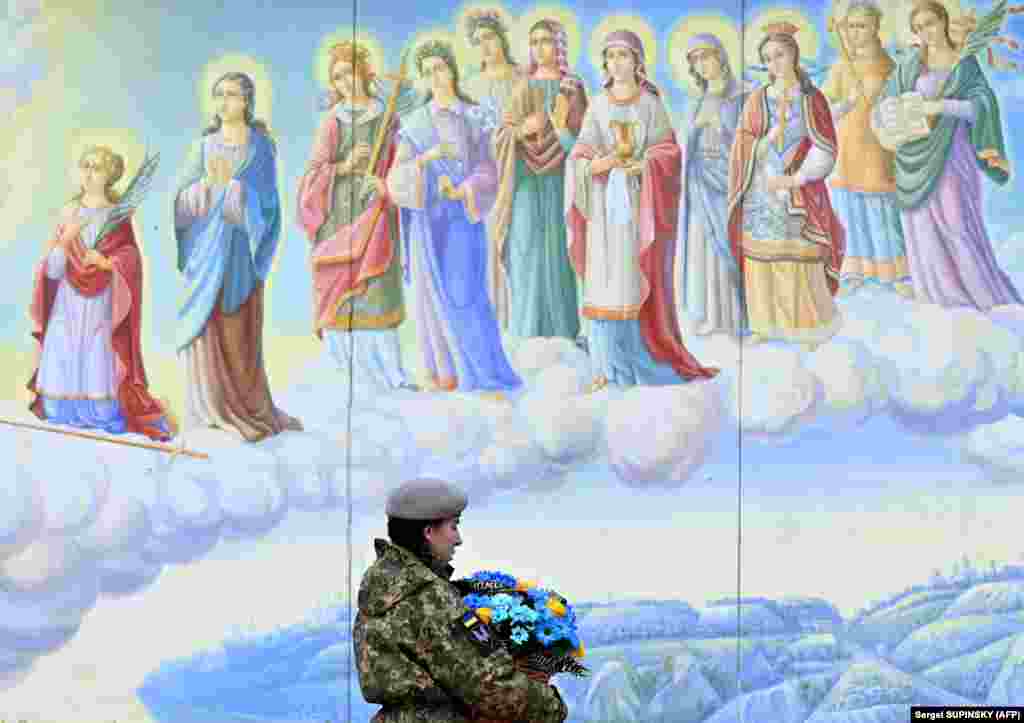 A Ukrainian soldier carries flowers in the colors of the Ukrainian flag as she walks in Kyiv to take part in the funeral service for a soldier killed in battle.