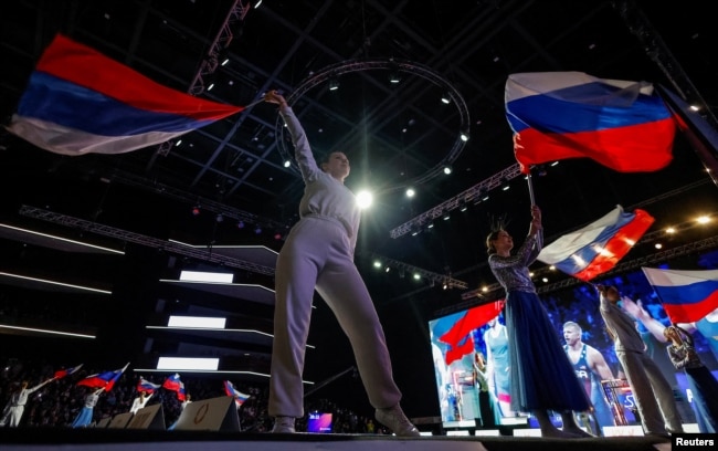 Учасники церемонії розмахують державними прапорами Росії під час офіційного відкриття чемпіонату Росії з вільної боротьби (етапу підготовки до Олімпійських ігор) у комплексі Live Arena поблизу Москви, 4 травня 2024 року