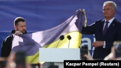 Президент Украины Владимир Зеленский и президент Литвы Гитанас Науседа на площади в Вильнюсе держат флаг Украины, который привезли из Бахмута во время акции в поддержку Украины в первый день саммита НАТО. Литва, 11 июля 2023 года