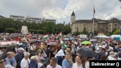 Eleredt az eső a tüntetés kezdetén, de gyorsan elállt. Tömeg a debreceni Kossuth téren, a Debreceni Református Nagytemplom előtt 2024. május 5-én