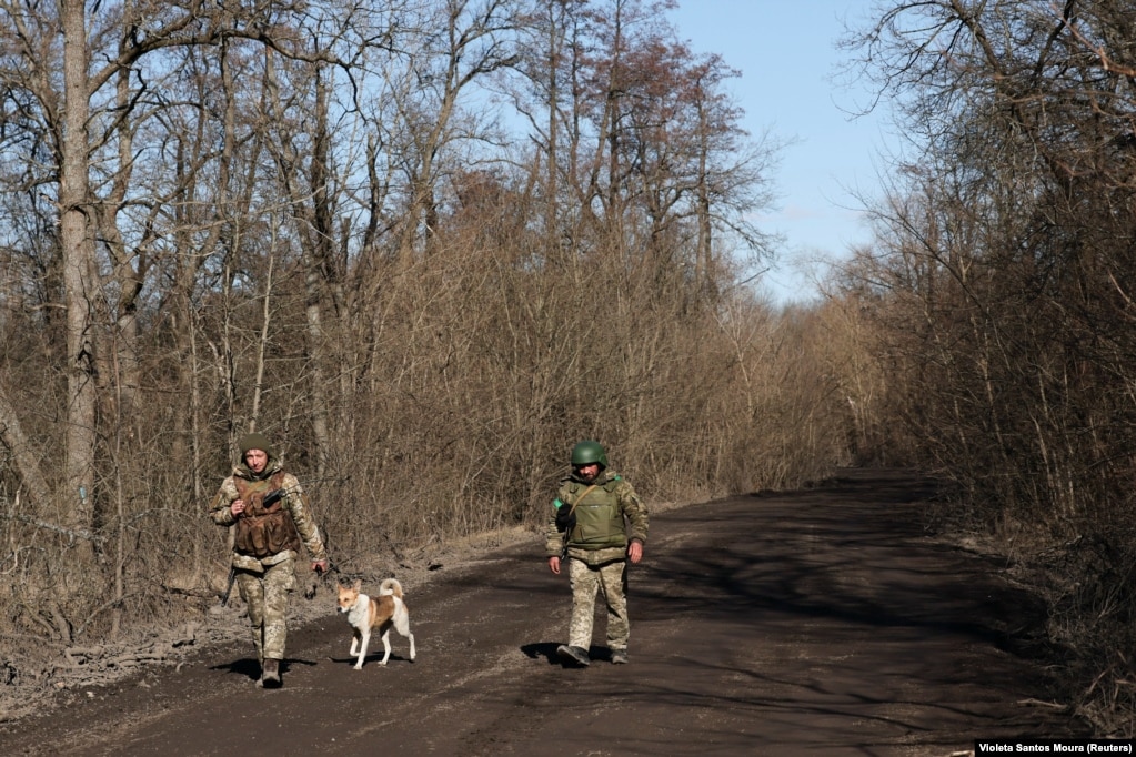 Ushtarët ukrainas duke ecur me qenin e njësisë së tyre në një vend të pazbuluar pranë qytetit të vijës së parë, Kremina, më 13 mars 2023.