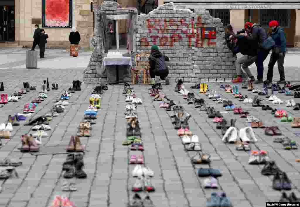 A woman sprays a sign on a wall next to shoes symbolizing the alleged war crimes committed against Ukrainian civilians by Russian forces in Ukraine at an installation in Old Town Square in Prague to mark the one-year anniversary of the Russian invasion.