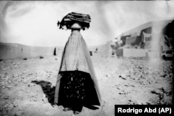 Një grua me burka shihet duke ecur drejt shtëpisë teksa bart me kokë bukë për familjen dhe fqinjët e saj në Bamiyan më 18 qershor.