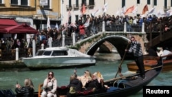 Imagine din Veneția, în epoca supraturismului: vizitatorii își fac selfie în gondolă, în timp ce deasupra lor sute de localnici protestează pentru a-și salva orașul.