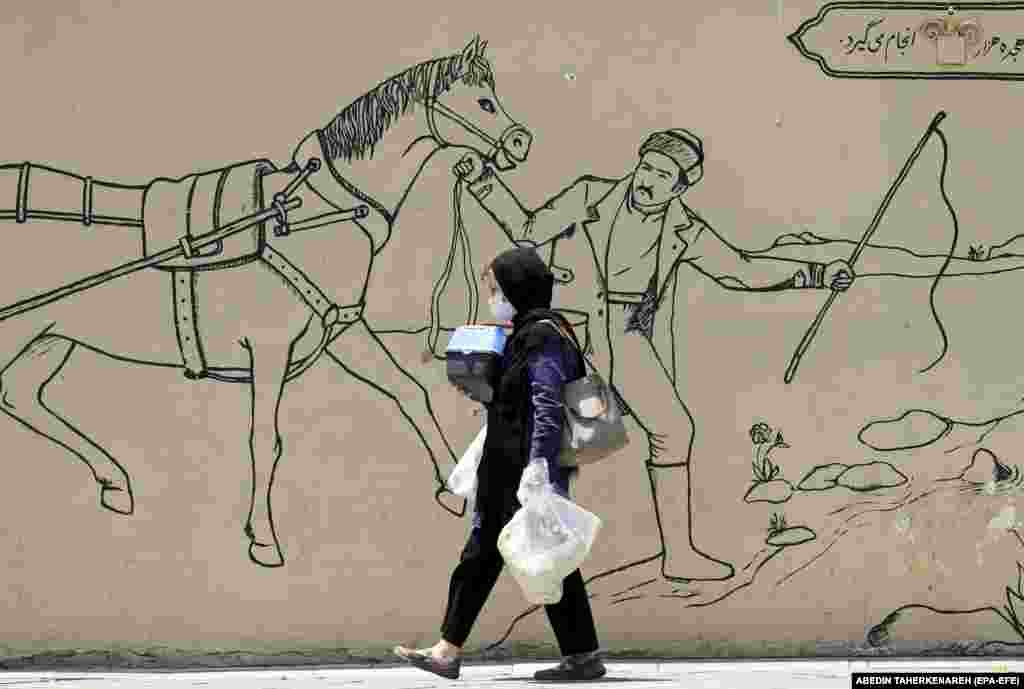 An Iranian woman walks past a wall painting in a street in Tehran.