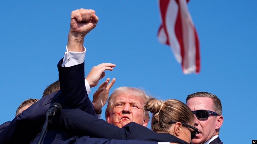 دونالد ترامپ در حلقه محافظانش در حالی که مشت خود را به سوی جمعیت بلند کرده و فریاد می‌زند