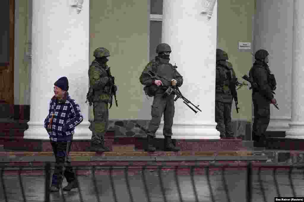 Российские солдаты, действующие без знаков различия, стоят возле аэропорта Симферополя, 28 февраля 2014 года. Российские солдаты-инкогнито появились по всему Крыму и стали известны как &laquo;зеленые человечки&raquo;. Кремль первоначально утверждал, что это были местные группы &laquo;самообороны&raquo;, но позже признал, что это были профессиональные российские солдаты.