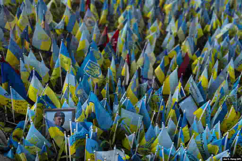 A photo of a Ukrainian soldier sits among Ukrainian flags bearing the names of people killed in Russian attacks at a memorial site in Kyiv.