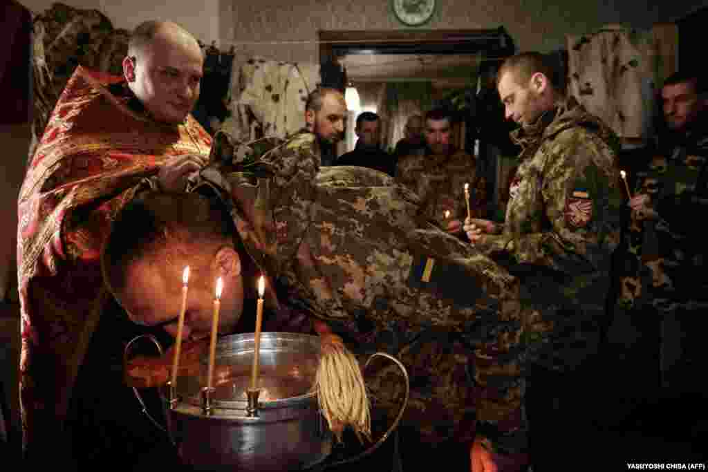 Mykola Berezyk (left), a chaplain to the Ukrainian Army, conducts a prayer for Ukrainian servicemen who returned from the front line as a serviceman kisses a cross in the Donetsk region.