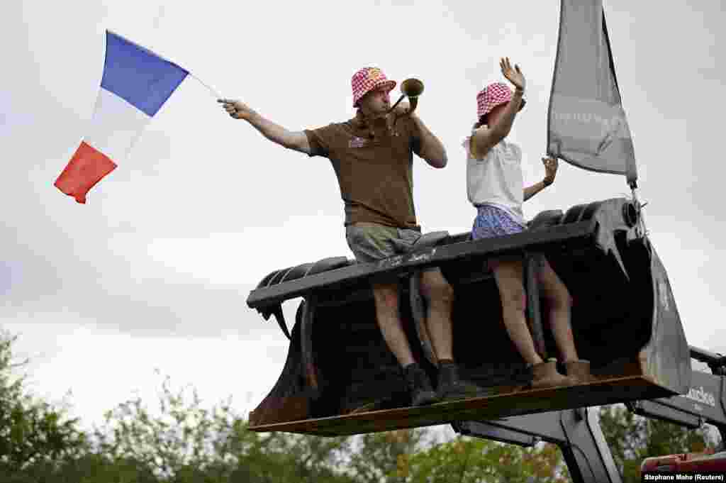 Spektatorë të hipur në ekskavatorë duke përshëndetur garuesit e Tour de France.