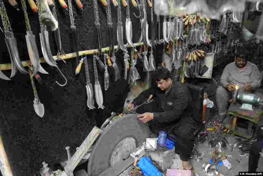 Ironsmiths sharpen their wares next to displays of knives and chains, sold for flagellating during Ashura, in Lahore, Pakistan.