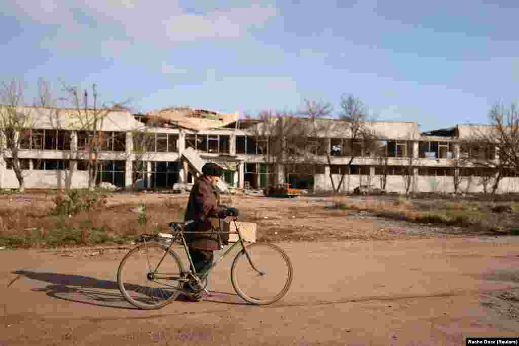 Мимо изуродованных войной зданий и ландшафта Владимир идет на велосипеде к пункту доставки, где волонтеры раздают еду последним оставшимся в селе жителям