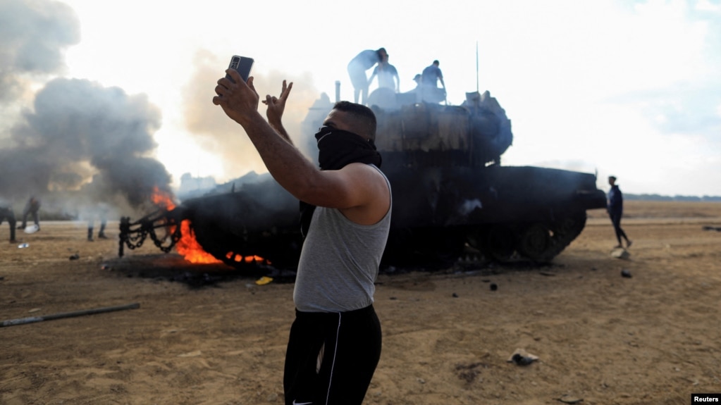 Житель Газы на фоне горящего израильского танка, 7 октября 2023 года