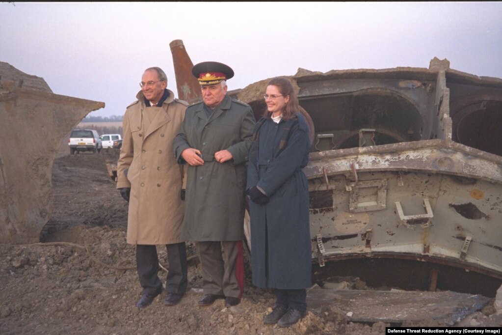 Roland Lajoie (majtas) dhe Laura Holgate (djathtas) nga Departamenti amerikan i Shtetit, duke pozuar me Volodymyr Mykhtyukun, komandant i një njësiti raketor ukrainas, i cili u shpërbë më 2002. Treshja shihet duke qëndruar pranë mbetjeve të një rakete në një vend të panjohur.