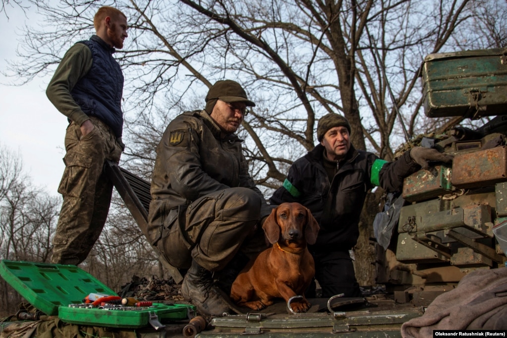 Një qen i quajtur Chip qëndron ulur pranë ushtarëve ukrainas ndërsa ata riparojnë një tank pranë&nbsp; vijës së parë të frontit në Bahmut, 20 janar 2023.
