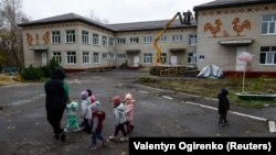 Učitelj sa djecom ispred vrtića oštećenog u granatiranju u prvim mjesima ruske invazije, u ukrajinskom gradu Okhtirka, na istoku države (2. novembar 2023.).