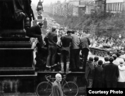 Această fotografie făcută de Paul Goldsmith din vârful Pieței Wenceslas, pe 21 august 1968. El a numit-o „Băieți pe bicicletă” și arată intrarea trupelor sovietice invadatoare, în timp ce un bărbat în costum trece întâmplător pe acolo în drum spre serviciu.