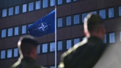 Шведські солдати дивляться, як прапор НАТО (справа) піднімається перед штабом збройних сил Швеції в Стокгольмі 11 березня 2024 року, символізуючи вступ Швеції до альянсу
