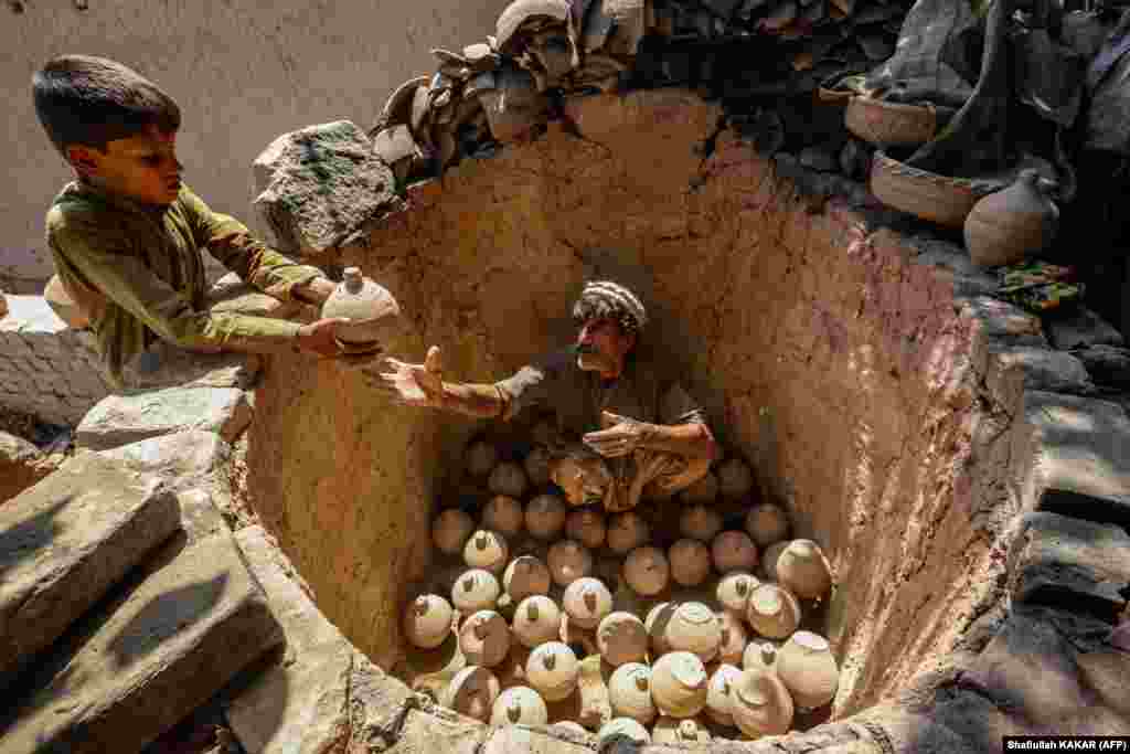 An Afghan boy helps a potter to sort clay piggy banks inside a kiln in Jalalabad.