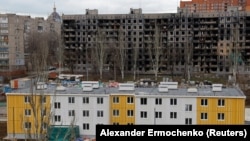 Kontraszt: újjonnan felhúzott lakóház, mögött egy kiégett szalagházzal Mariupolban, 2023. február 15-én.