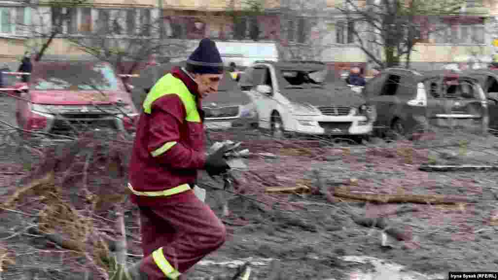A city employee begins clearing up near shattered cars in a residential parking lot.