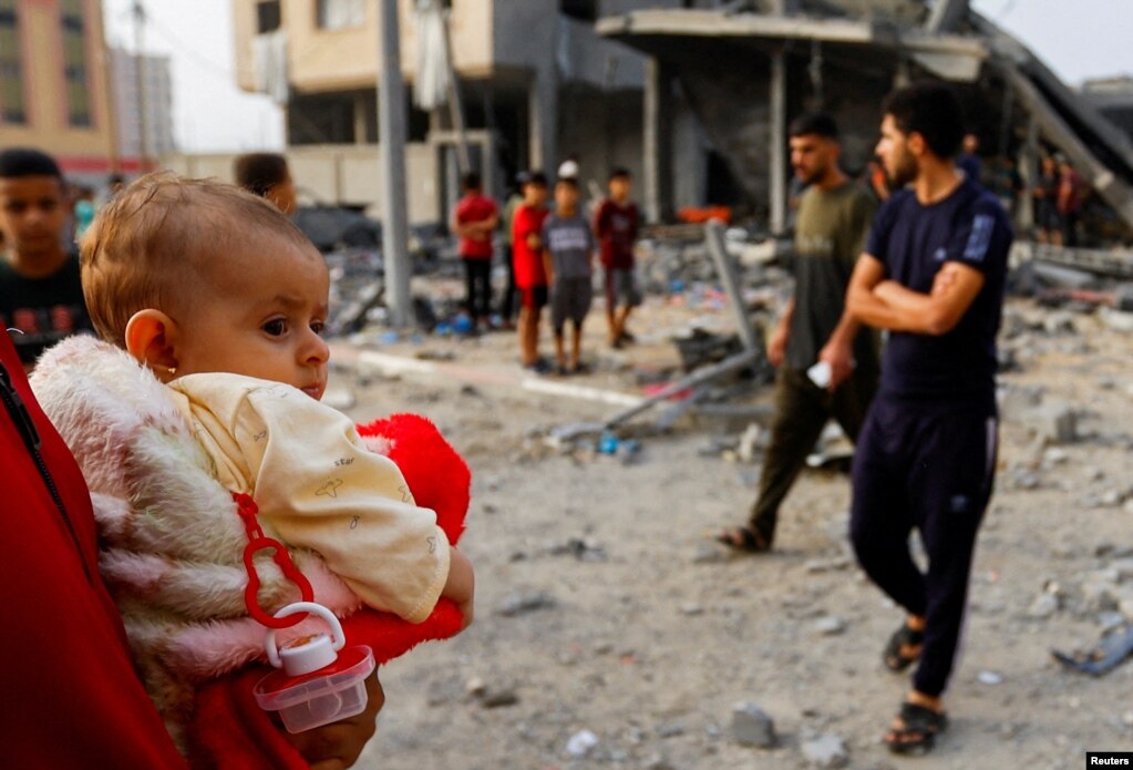 Një person mban në duar një fëmijë ndërsa palestinezët mblidhen në vendin e sulmeve izraelite në një shtëpi në Han Junis, Rripi i Gazës, 23 tetor 2023.