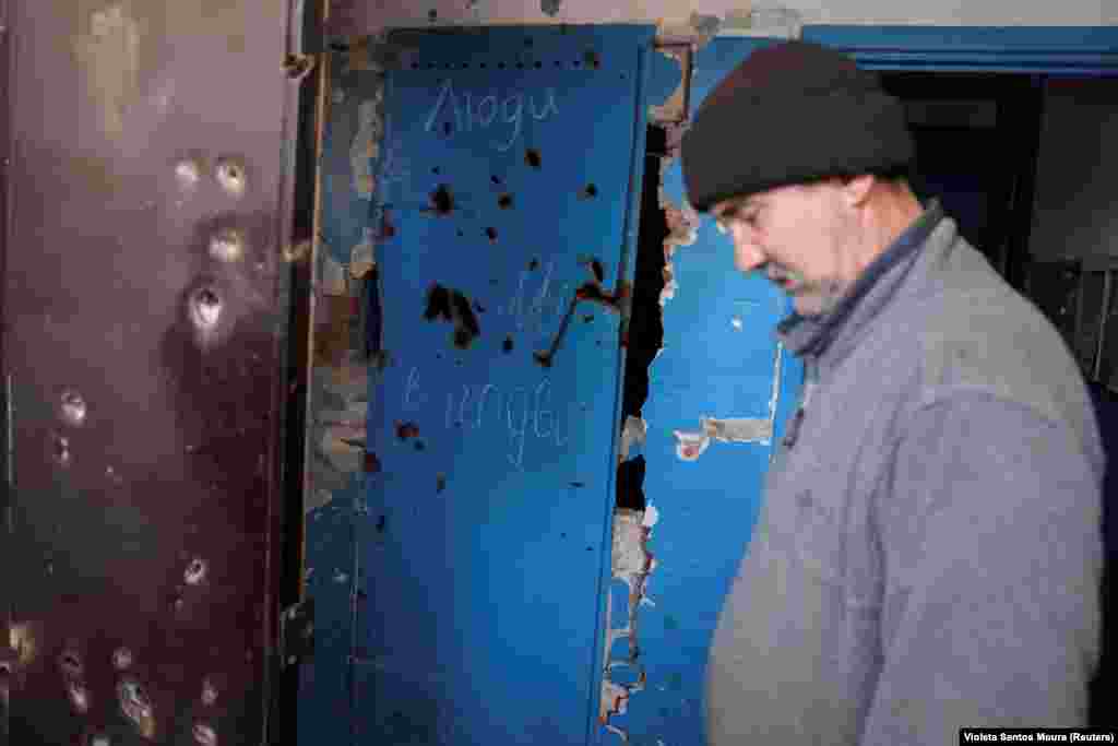 Basement doors show shrapnel damage and writing announcing the presence of civilians. Volodymyr, 56, listens as volunteers try to persuade civilians like him to leave Chasiv Yar.