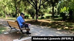 Pripadnik starije populacije sjedi na klupi u parku u Podgorici