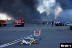 Тело погибшего на фоне горящего гипермаркета "Эпицентр" в Харькове после росийского удара двумя авиабомбами, 25 мая 2024 года