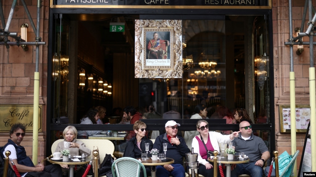 Njerëzit të ulur jashtë një restoranti ku shihet një fotografi e Mbretit Charles.