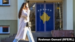 Një vajzë duke kaluar pranë një vitrine ku është varur flamuri i Kosovës.
