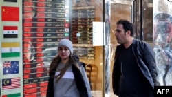 Dy persona kalojë pranë një këmbimoreje në Teheran. Sanksionet e OKB-së pritet të godasin ekonominë iraniane, përfshirë edhe dobësimin e valutës së shtetit. 