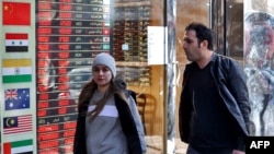 People walk past a currency exchange shop in Tehran. UN snapback sanctions are expected to hit the Iranian economy, including the value of the country's currency, the rial. 