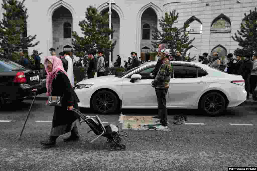 Пожилая женщина с тележкой проходит мимо молящихся у мечети мусульман