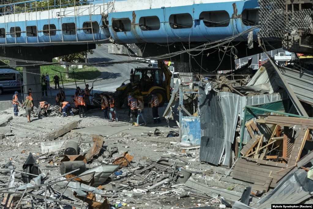 Punonjësit komunalë duke pastruar vendin e një zone të goditur nga një sulm ushtarak rus në Dnipro, Ukrainë.