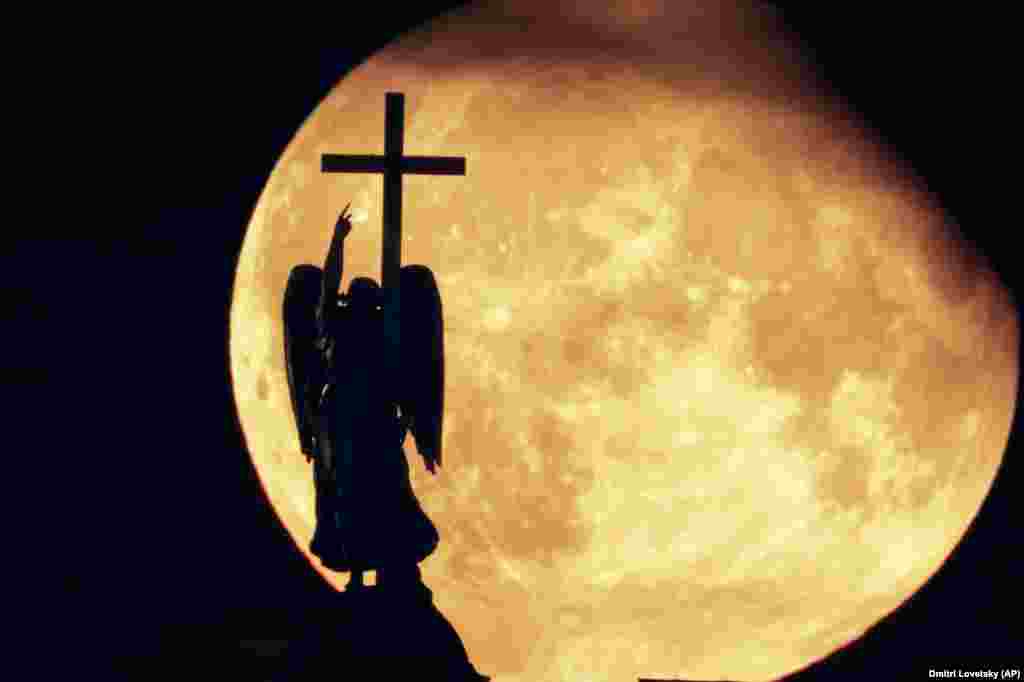 A supermoon known as the Sturgeon Moon rises in the clouds behind a statue of an angel fixed atop the Alexander Column at Palace Square in St. Petersburg, Russia, on August 1.