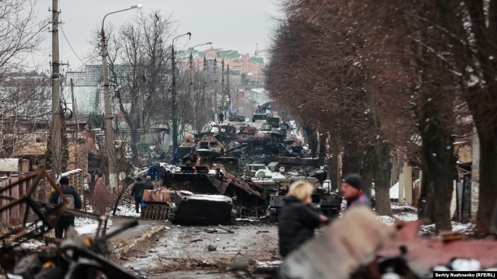 Civilët shikojnë një kolonë automjetesh të blinduara ruse të shkatërruar në Buça, afër Kievit, më 1 mars 2022. Qyteti u kap nga trupat ruse disa ditë pasi u bë kjo foto, por ato u tërhoqën më pak se një muaj më vonë. Pas tërheqjes së Moskës, dolën në pah provat e krimeve të luftës në Buça, duke tërhequr dënimin ndërkombëtar.