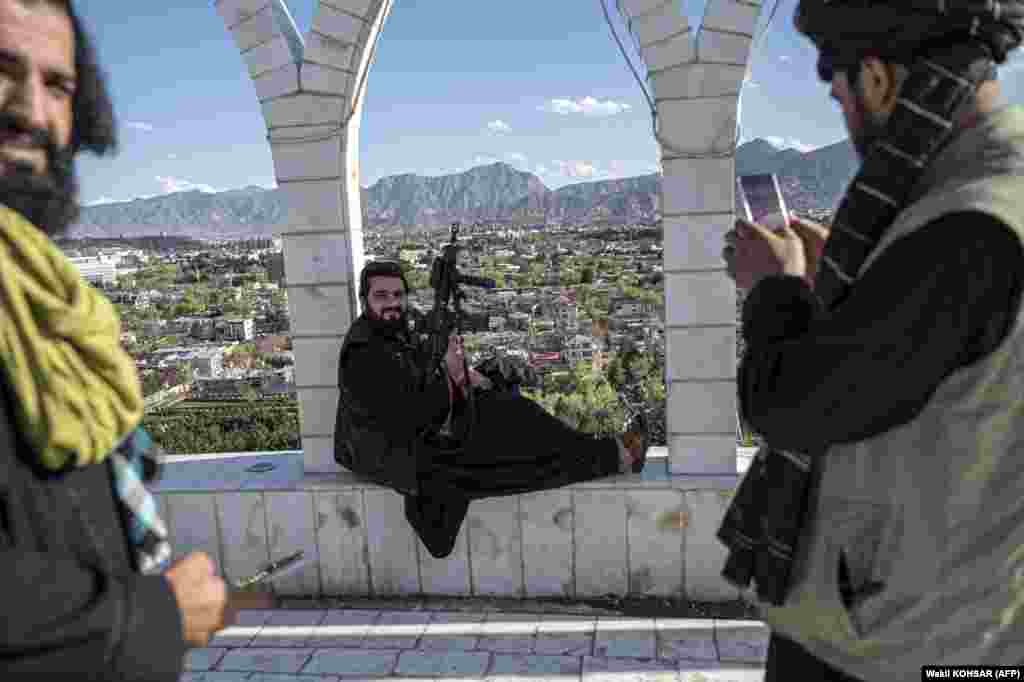 Un ofițer de securitate taliban își fotografiază colegul cu un telefon mobil, pe fundalul vârfului Wazir Akbar Khan, care domină capitala afgană, Kabul.