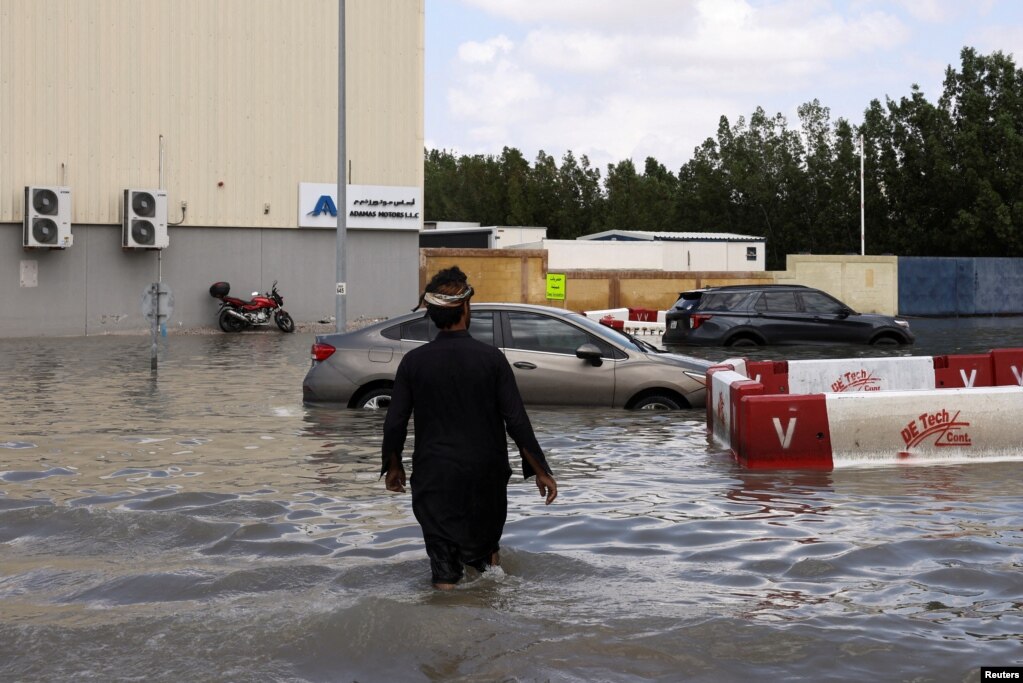 Një burrë duke ecur drejt makinave të bllokuara në ujërat e përmbytjeve të shkaktuara nga shiu i dendur në Dubai, Emiratet e Bashkuara Arabe, 17 prill 2024. Punonjësit e ekipeve emergjente filluan të pastronin rrugët pasi një stuhi e rrallë shkaktoi përmbytje në Emiratet e Bashkuara Arabe.  