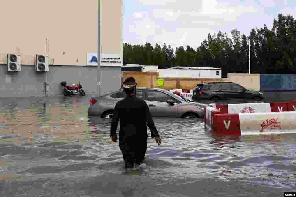 Një burrë duke ecur drejt makinave të bllokuara në ujërat e përmbytjeve të shkaktuara nga shiu i dendur në Dubai, Emiratet e Bashkuara Arabe, 17 prill 2024. Punonjësit e ekipeve emergjente filluan të pastronin rrugët pasi një stuhi e rrallë shkaktoi përmbytje në Emiratet e Bashkuara Arabe. &nbsp;