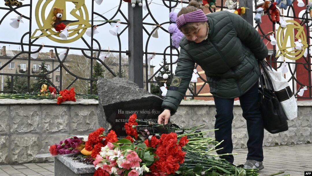 A woman lays flowers at a memorial near the train station in Kramatorsk in Ukraine's Donetsk region where dozens of civilians were killed by a Russian missile strike one year ago. 