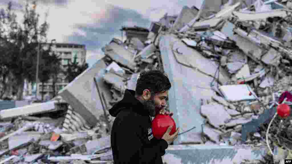 Ogun Sever Okurt duke fryrë balona mbi mbeturinat e një ndërtese të shembur në Antakya, Turqia jugore më 21 shkurt 2023.
