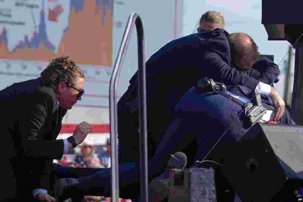 Trump is covered up by U.S. Secret Service agents on stage at a campaign rally after shots are heard.