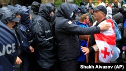Tbilisidə müxalifətin "Xarici agent" qanununa etiraz zamanı aksiyaçı parlament binasına gedən yolu bağlayan polislə mübahisə edir.